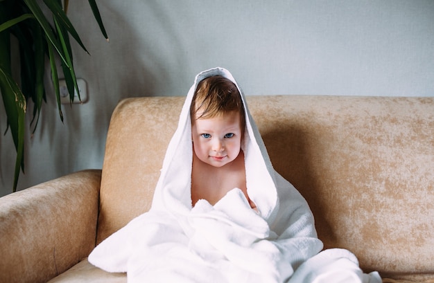 Enfant mignon aux yeux bleus enveloppé dans une serviette blanche