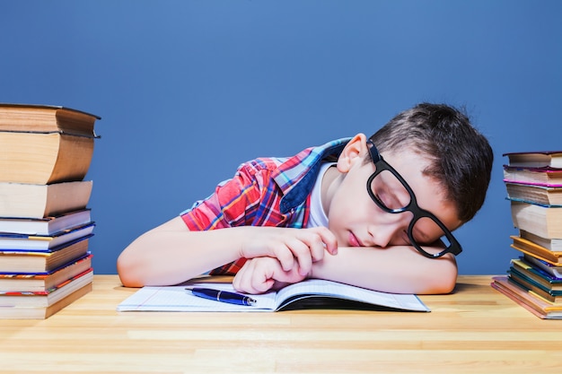 Enfant mignon endormi au bureau dans la bibliothèque de l'école. Élève dans des verres contre de nombreux livres