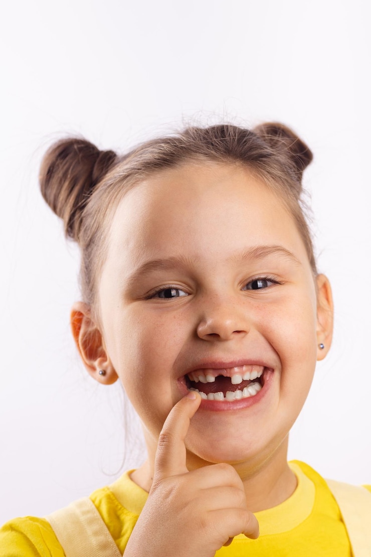 Photo enfant mignon femelle avec la bouche ouverte montrant la dent avant manquante avec le doigt sur la lèvre inférieure souriant en t-shirt jaune sur fond blanc premiers changements de dents aller chez le dentiste pour faire un traitement dentaire