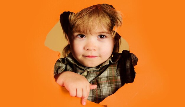 Enfant mignon jetant un coup d'œil à travers le trou dans la bannière publicitaire en papier vente de saison de réduction d'enfance heureuse