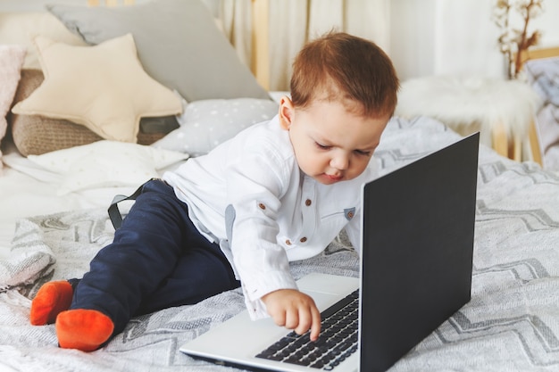 Enfant mignon avec un ordinateur portable sur le lit