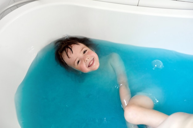 Enfant mignon se baignant dans l'eau bleue dans la baignoire