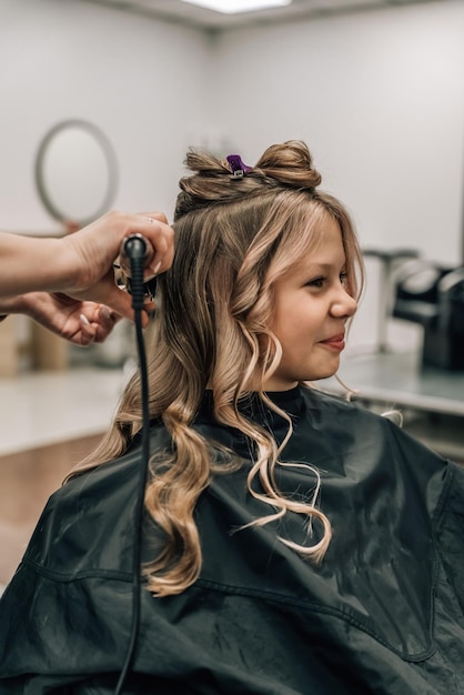 Enfant mignon se coiffer Coiffeur avec fer à friser Génération de la mode