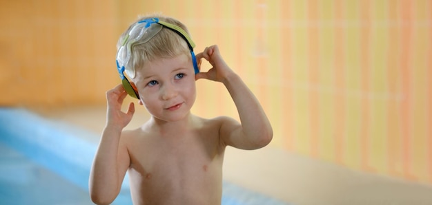 Enfant mignon tout-petit près de la piscine souriant dans des lunettes après avoir nagé