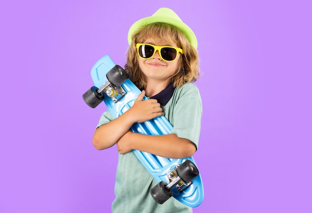 Enfant de mode en chemise d'été chapeau élégant et lunettes de soleil Enfant mignon avec planche à roulettes sur fond isoalté de couleur Patineur élégant enfant garçon drôle tenant planche à roulettes en studio