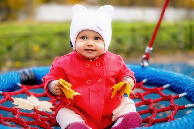 Enfant monte sur une balançoire avec des feuilles d'automne jaunes