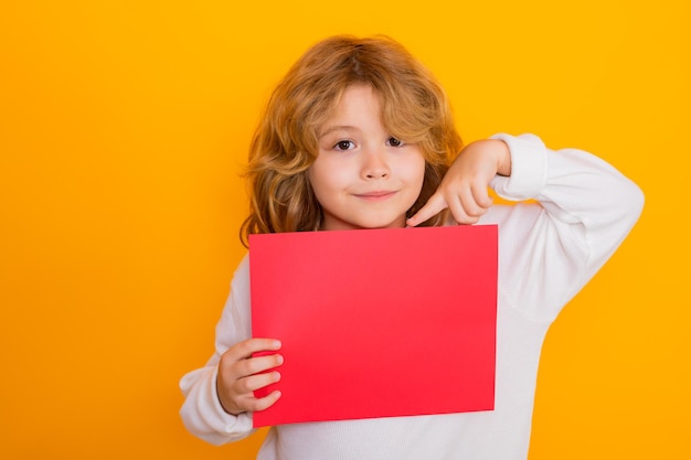 Enfant montrant l'index sur une feuille de papier rouge isolé sur fond jaune portrait d'un enfant hol
