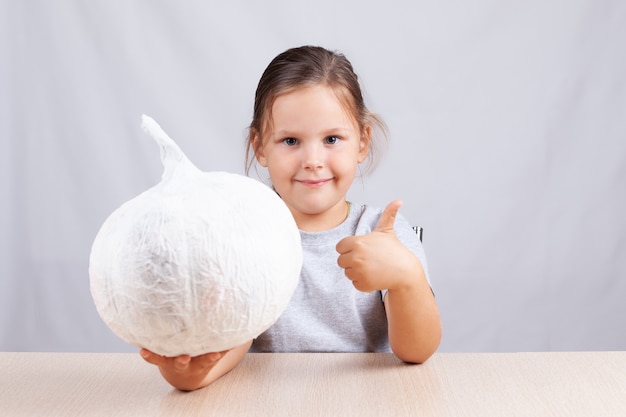 L'enfant montre les pouces vers le haut et tient une serviette de table à la citrouille faite maison et des décorations en papier pour Halloween.