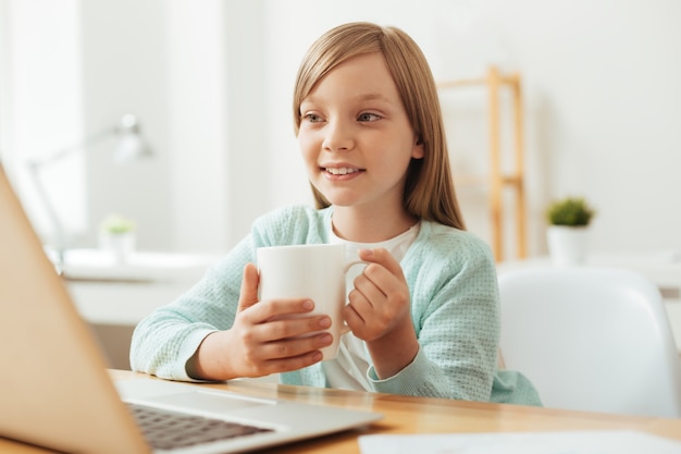 Enfant à motivation intelligente analytique assis à la table et regarder des dessins animés à l'aide de son ordinateur portable