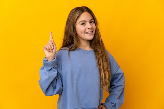 Enfant sur mur jaune isolé montrant et levant un doigt en signe du meilleur