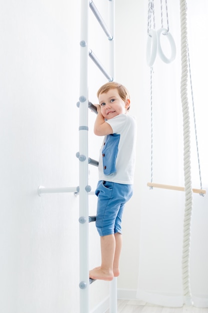 Un enfant sur le mur suédois fait du sport à la maison, un garçon monte une échelle avec une corde, le concept de sport et de santé