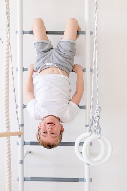 Un enfant sur le mur suédois fait du sport à la maison, un garçon monte une échelle avec une corde, le concept de sport et de santé