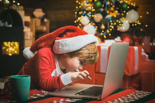 Enfant de Noël garçon tapant une lettre au père noël sur un ordinateur portable à la maison sur fond de noël