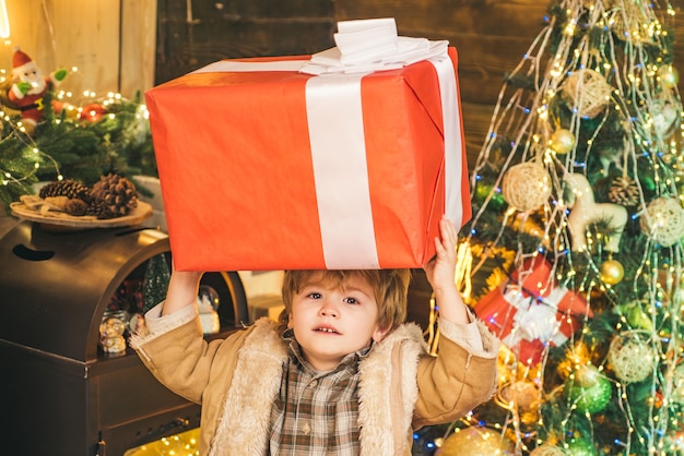 Enfant de Noël tenant une énorme boîte-cadeau enfant heureux décorant l'arbre de noël enfant mignon heureux dans sa...