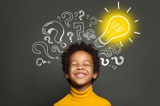 Photo un enfant noir heureux sur fond noir avec une ampoule et des points d'interrogation brainstorming et concept d'idée