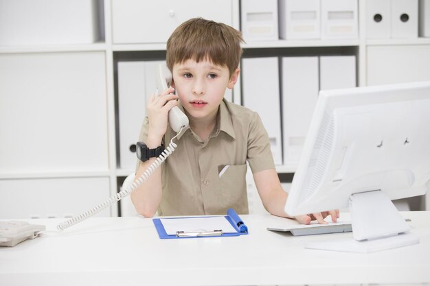 L'enfant à l'ordinateur tenant le téléphoneEnfant homme d'affaires au bureauGarçon jouant à l'homme d'affaires