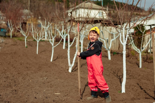 Un enfant avec un outil de jardin dans un potager à côté d'arbres de jardin travaille et aide à planter des arbres un