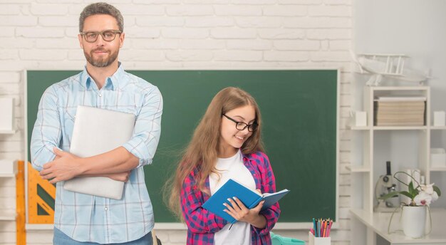 Enfant et papa en classe avec cahier et ordinateur à l'étude du tableau noir