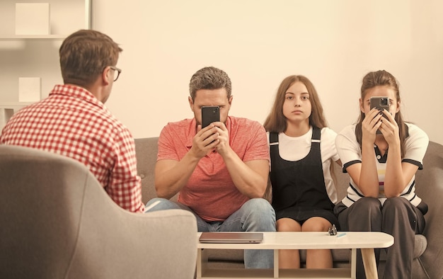 Enfant avec papa et maman accros au téléphone assis chez un psychologue résolvant une relation problématique