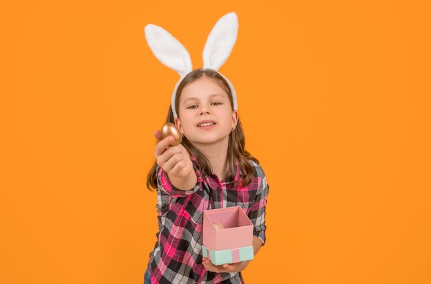 L'enfant de Pâques dans les oreilles de lapin tient la boîte et l'oeuf sur fond jaune