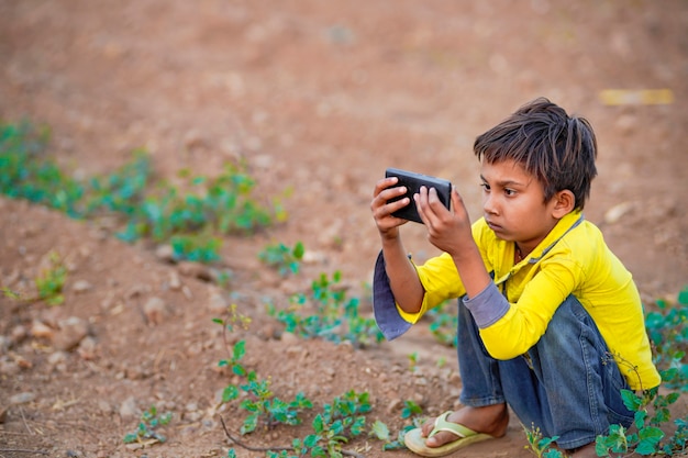 Enfant pauvre indien jouant avec un mobile sur le terrain agricole. Scène rurale.