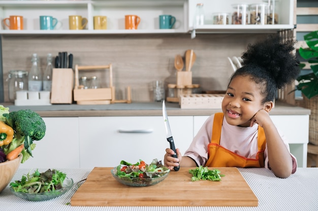 Enfant à peau noire avec salade sur assiette dans la cuisine