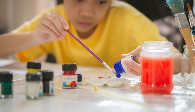 Enfant peignant à table dans la salle de jeux, fille avec pinceau et peinture à la palette, Apprentissage de la peinture en ligne