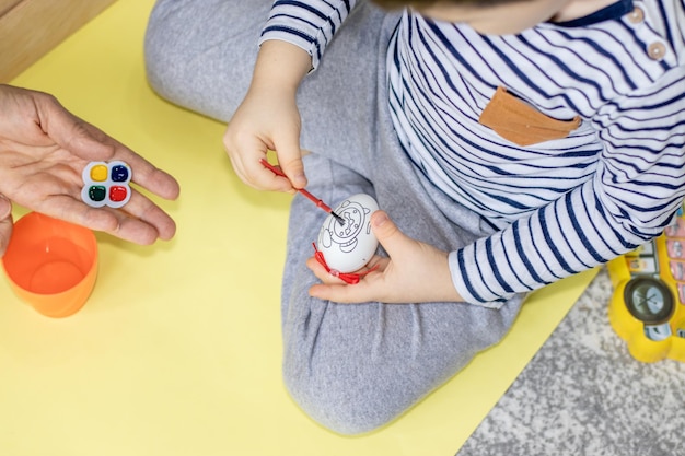 un enfant peint un oeuf de pâques à l'aquarelle aidé par les activités de la maison de vacances de pâques de grand-mère