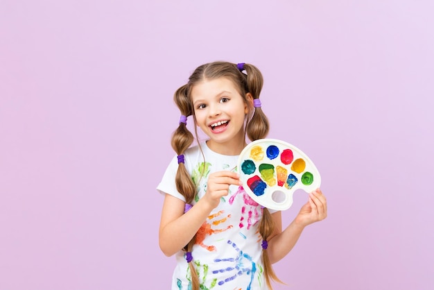 Un enfant avec des peintures sur un fond isolé une petite fille dans un T-shirt avec des empreintes de mains avec des peintures une passion pour la peinture