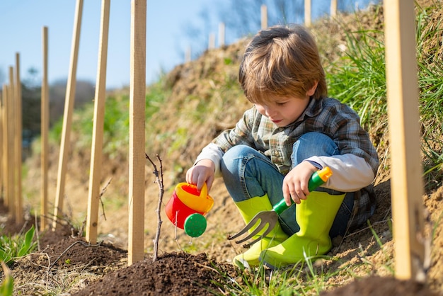 Enfant avec pelle et arrosoir Mignon petit garçon arrosant la pousse sur le terrain Petit garçon profiter des années d'enfance à la ferme