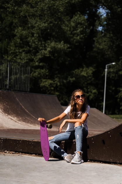 Enfant avec penny board Jeune fille adolescente dans des verres avec skate board assis sur une rampe de sport sur une aire de skate Mode de vie extrême Publicité créative pour skate ou penny board magasins ou magasins