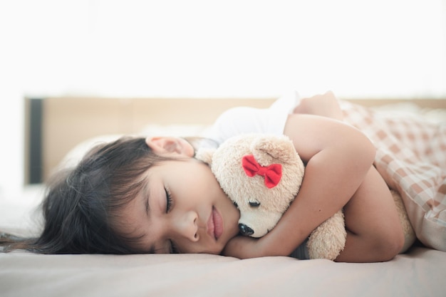 Enfant petite fille dort dans le lit avec un ours en peluche jouet