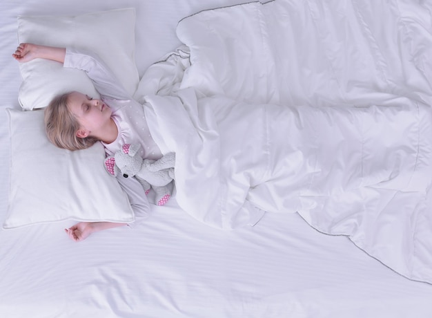 Enfant petite fille dort dans le lit avec un ours en peluche jouet