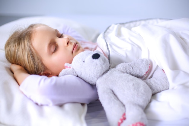 Enfant petite fille dort dans le lit avec un ours en peluche jouet