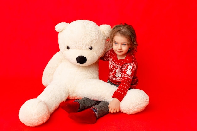 Enfant une petite fille avec un gros ours en peluche dans des vêtements d'hiver sur un espace de fond rouge pour le texte