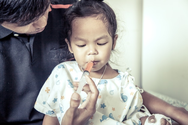 Enfant petite fille obtient des médicaments avec une seringue dans sa bouche dans le ton de couleur vintage