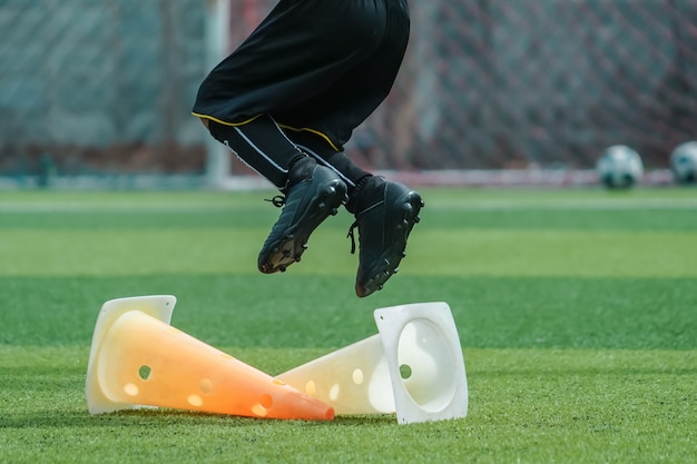 Enfant pieds pratique Sauter par-dessus le cône sur le terrain de football