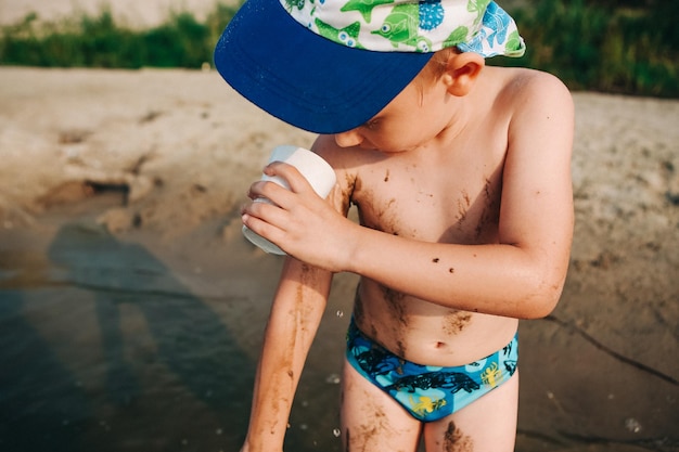 Un enfant sur la plage se lave le corps avec une tasse d'eau du sablexDxA