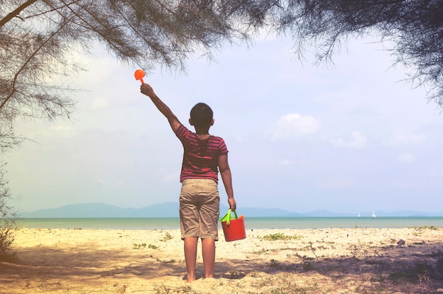 Enfant avec la plage et un seau de sable à la main.