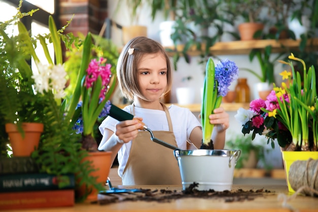 Enfant plantant des fleurs de printemps. Petite fille jardinier plante jacinthe. Fille tenant la jacinthe en pot de fleur. Enfant prenant soin des plantes. Outils de jardinage. Copiez l'espace.