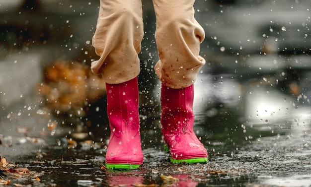 Enfant portant des bottes en caoutchouc debout dans une flaque d'eau en jour de pluie à l'automne. Pieds d'enfant dans des bottes en caoutchouc à l'extérieur en automne