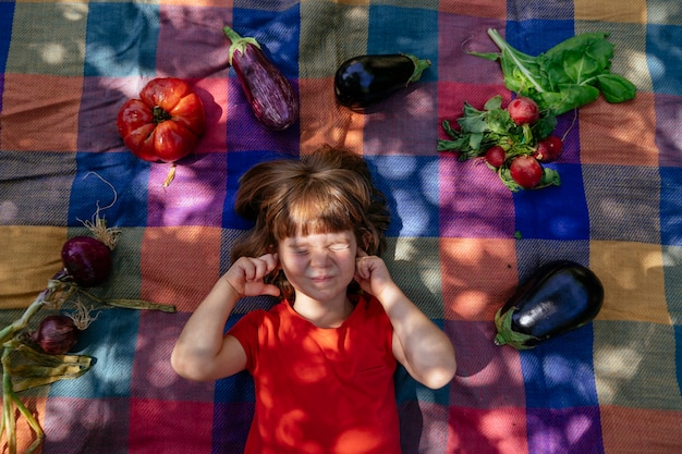 Enfant portant sur une couverture à carreaux à l'extérieur avec des légumes