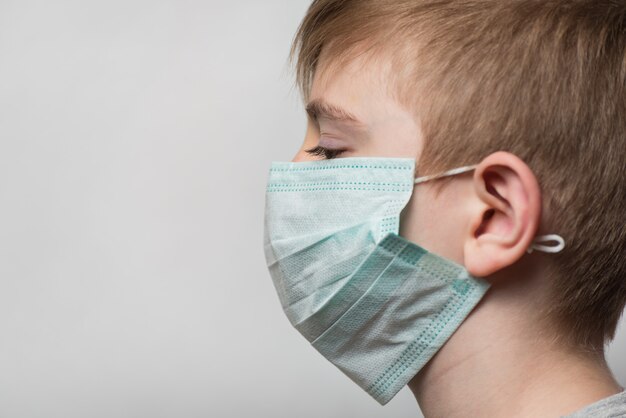 L'enfant porte un masque médical pour se protéger des germes. Portrait Vue latérale.