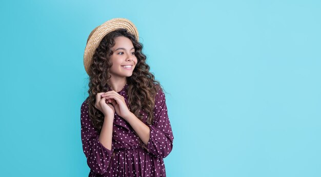 Enfant positif au chapeau de paille avec de longs cheveux bouclés brune sur fond bleu