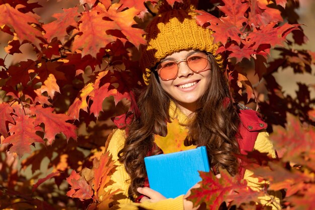 Enfant positif tenir livre sur fond de feuilles d'automne