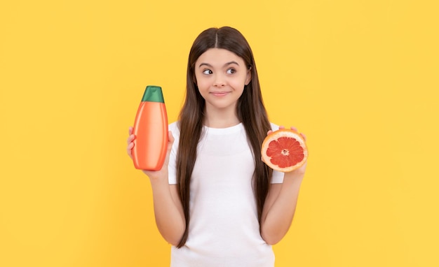 Un enfant positif tient une bouteille de revitalisant pour les cheveux et un pamplemousse sur une publicité de fond jaune