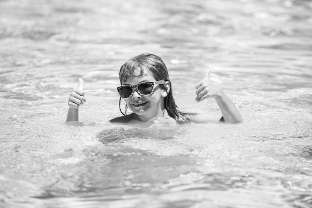 Enfant avec les pouces vers le haut dans les lunettes de soleil se détendre dans la piscine d'été enfants actifs mode de vie sain eau