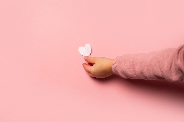 L'enfant prend une carte de la Saint-Valentin en papier sur fond rose. Composition Saint-Valentin. Bannière. Mise à plat, vue de dessus.