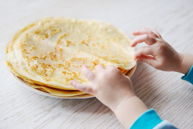 Enfant prend une crêpe d&#39;une assiette avec des crêpes