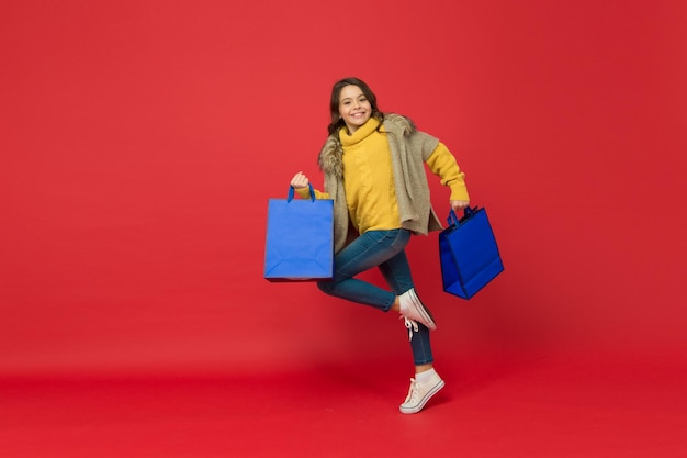 Un enfant pressé porte des sacs à provisions et court pour une grande vente dans un magasin accro du shopping